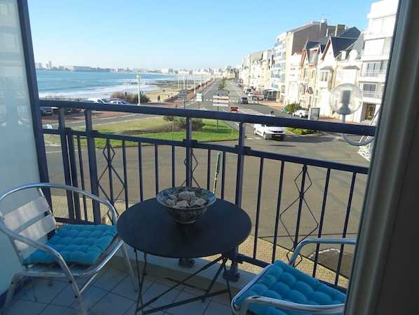 A balcony with a table and chairs, overlooking a street with buildings and a beach. - Seafront studio in Les Sables-d'Olonne, pet-friendly (Les Sables-d'Olonne)