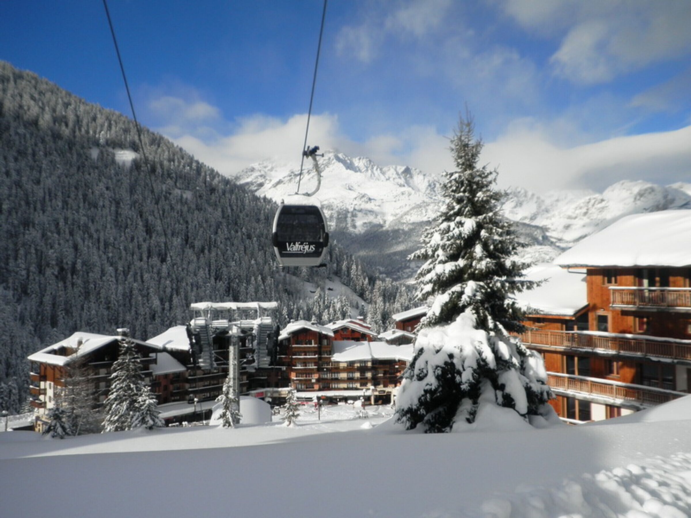 A ski lift with cabins, a wooden lodge, and snow-covered mountains in the background.