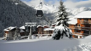Un télésiège avec des cabines, un chalet en bois et, au loin, des montagnes enneigées.