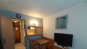 Une pièce de taille modeste comprenant une table à manger, des chaises, un téléviseur, une petite kitchenette et un tableau accroché au mur.