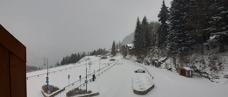 A snowy mountain road with a car parked on the side, surrounded by trees and buildings.