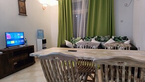 Un salon avec une table en bois, des chaises, un téléviseur et un distributeur d’eau.