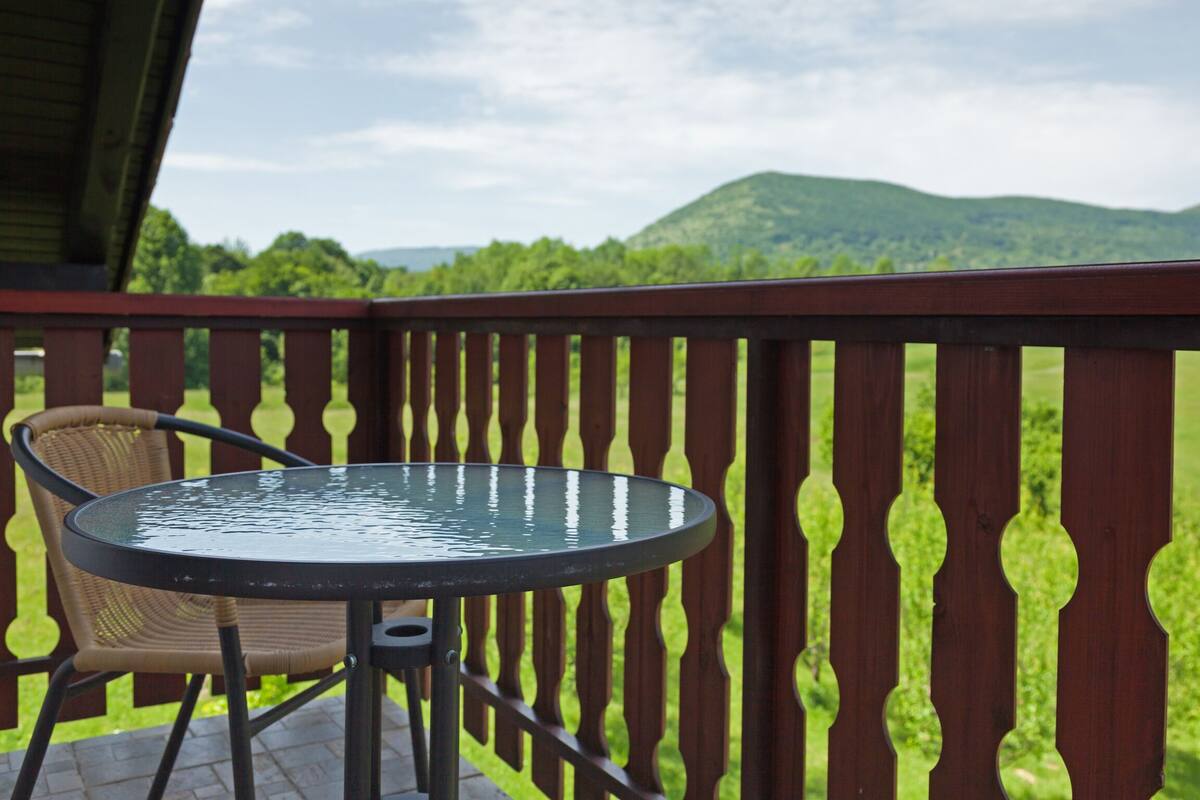 Eine Terrasse mit Tisch und Stuhl, mit Blick auf eine grüne Landschaft mit Hügeln.