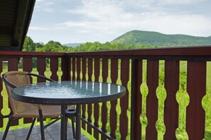 A deck with a table and chair, overlooking a green landscape with hills. - Guesthouse Žafran (Plitvicka Jezera)