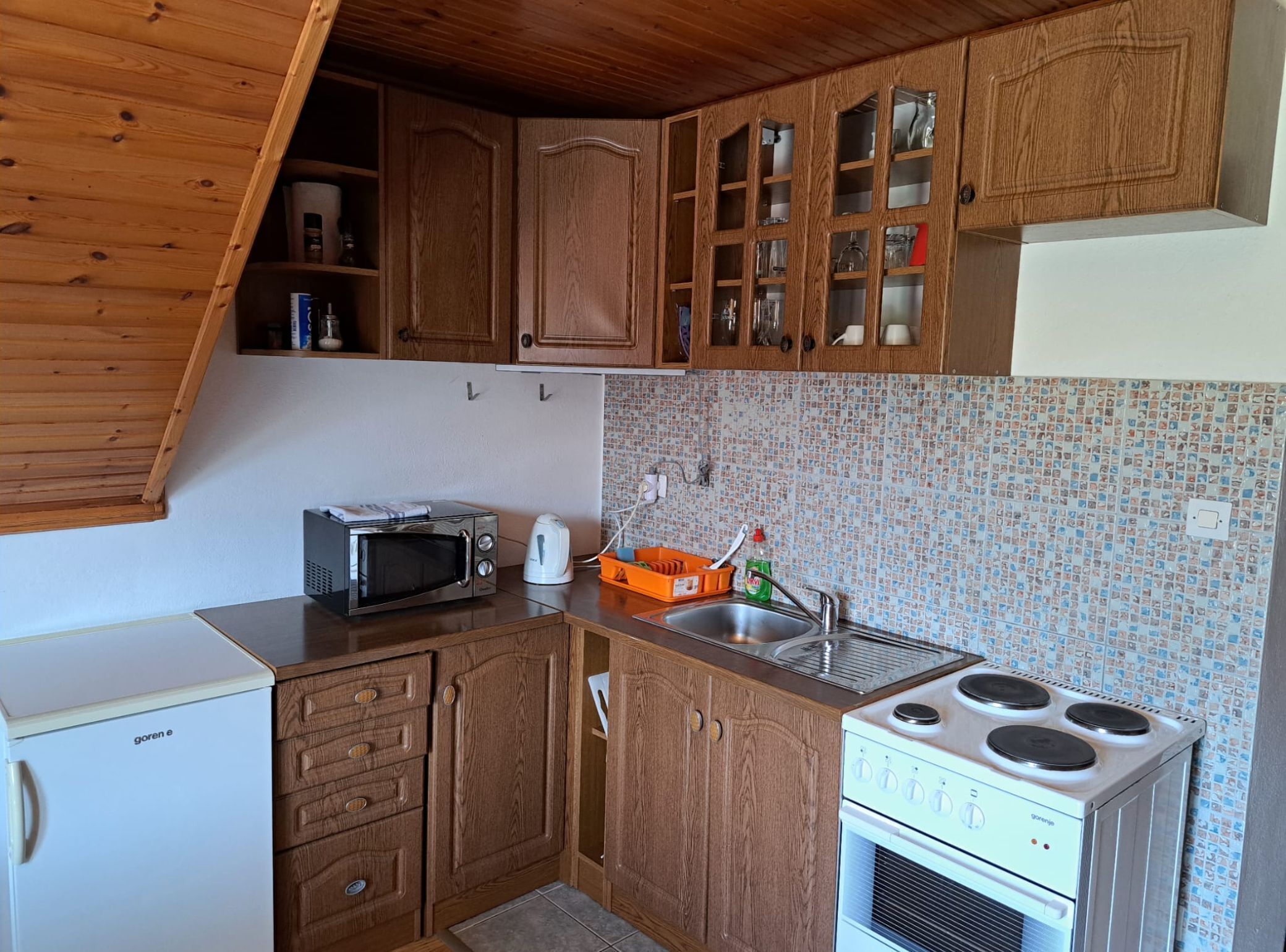 Una cocina compacta con armarios de madera, microondas, hervidor y estufa.