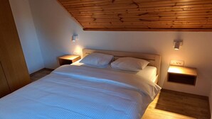 Et soveværelse med træloft, en stor seng med hvide sengetøj, to sengeborde med lamper og en trægulv.