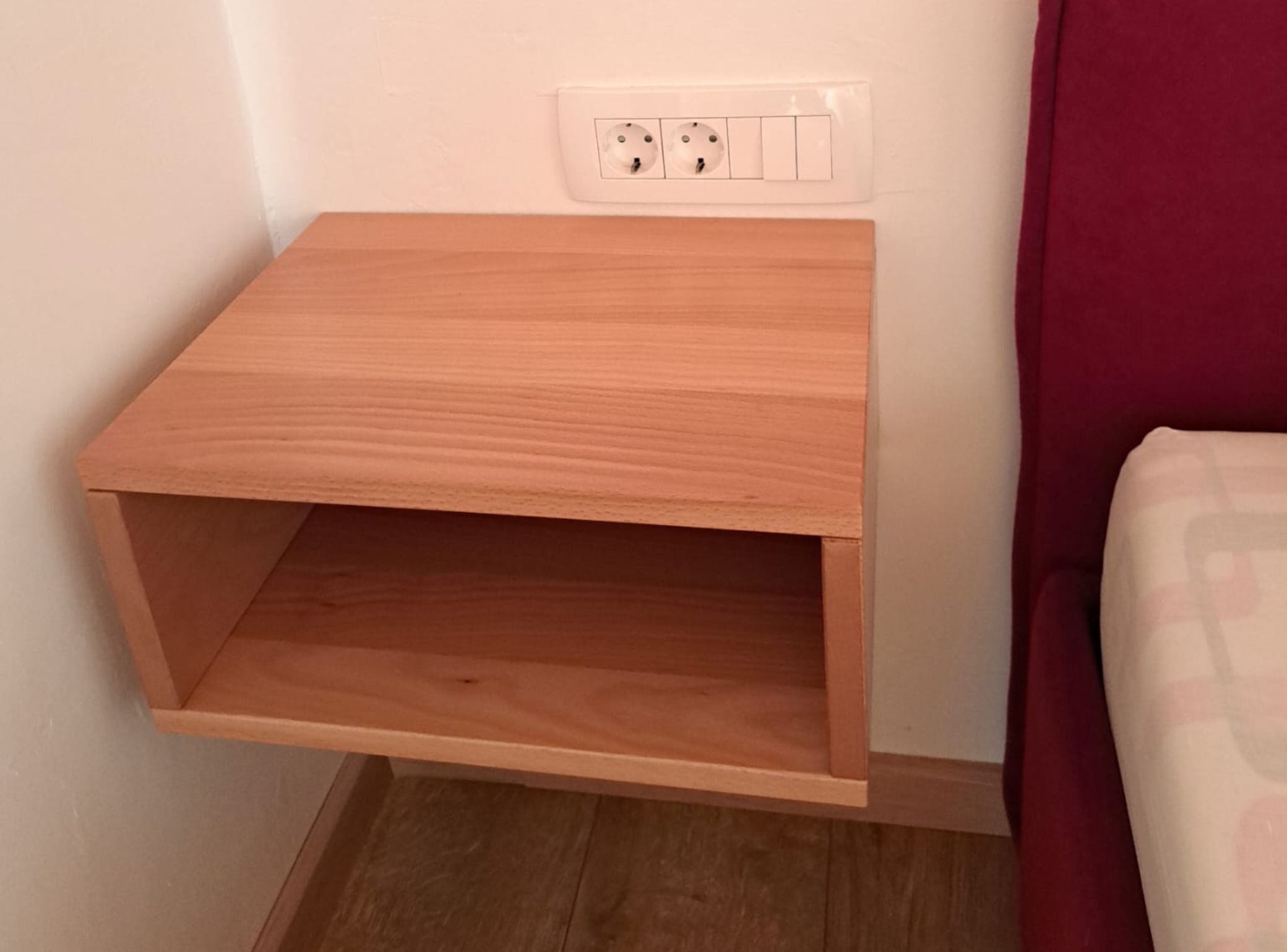 Puisesta yöpöydästä, jossa on hylly, ja se on sijoitettu seinän pistorasian viereen.