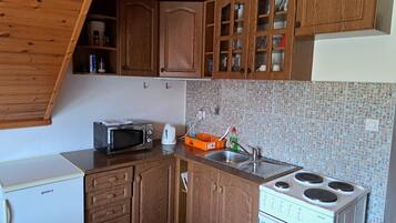 Una cocina compacta con armarios de madera, microondas, hervidor y estufa.