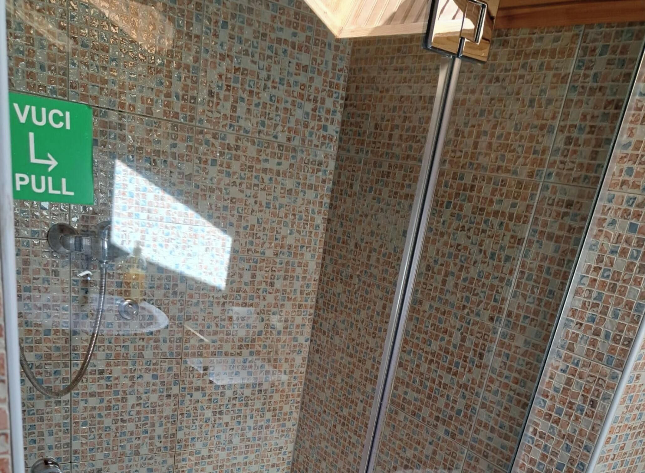 A shower area with mosaic tile walls, a glass door, and a 'VULI PULL' sign.