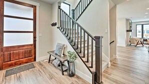 Una escalera moderna con detalles de madera y barandillas metálicas, que conduce a un espacio interior bien iluminado con un banco y una planta en maceta cerca de la entrada.