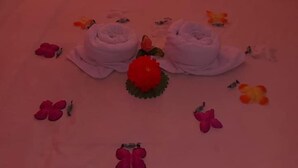A bed with two white towels folded at the center, surrounded by red and pink flowers. - Broad Park Hotel (Mbale)
