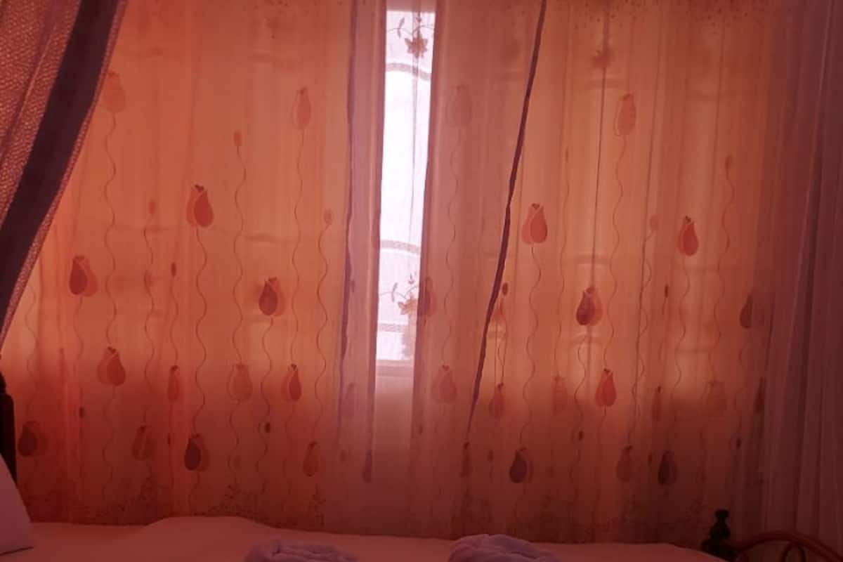 Cama bem arrumada com toalhas e flores, janela com cortinas leves e a estrutura da cama.