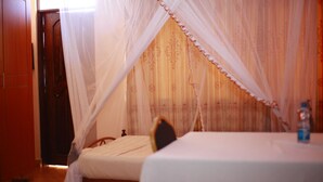 A room with a bed under a canopy, a wooden door, and a table with a bottle. - Broad Park Hotel (Mbale)