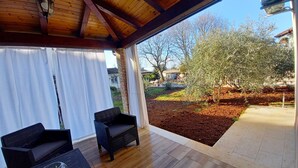 An outdoor patio with wooden flooring, two wicker chairs, and a glass table. - Holiday house on peaceful location in the suburb of Pula (Pula)