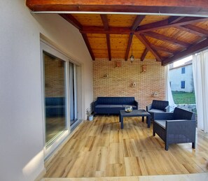 Eine überdachte Terrasse mit Holzboden, einem dunkelgrauen Sofa, zwei Sesseln und einem kleinen Tisch.