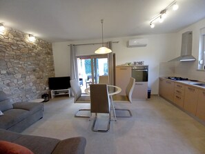 Ein modernes Wohnzimmer mit Steinwand, Flachbildfernseher, einer Couch und einem Essbereich mit Tisch und Stühlen.