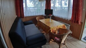 A cozy room with a sofa, a table with a floral tablecloth, wicker chairs, and a television on a stand.