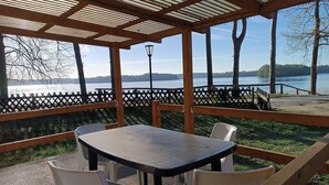 A covered outdoor seating area with a table and chairs, overlooking a lake.