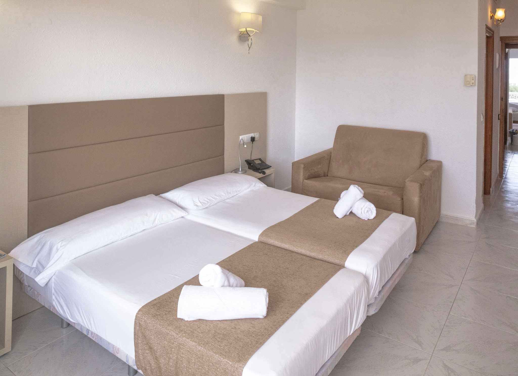 Habitación de hotel con una cama grande, una silla y una mesita de noche con lámpara.