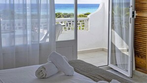 A hotel room with a bed, a window with sheer curtains, a view of the ocean, and a balcony with a white railing. - Roquetes Rooms - Formentera Break (Formentera)