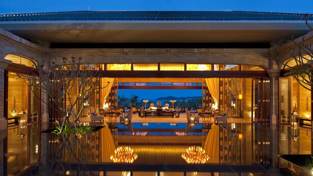 Un hall d’hôtel luxueux avec un bassin aux reflets scintillants, des fauteuils élégants et une vue panoramique sur les montagnes.