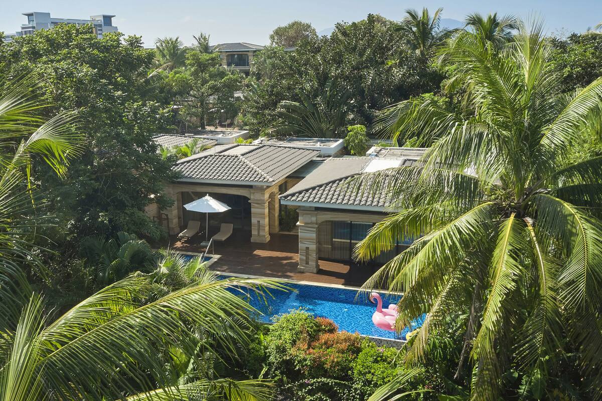 Un espace piscine agrémenté d’un flotteur en forme de flamant rose, entouré d’une végétation luxuriante et doté d’un patio couvert avec des meubles d’extérieur.