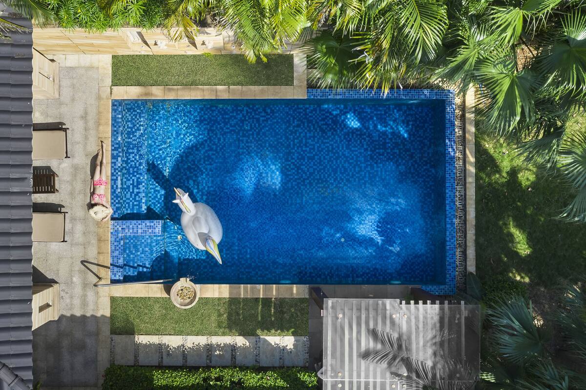 Vue aérienne d’une piscine rectangulaire dont le fond est carrelé, entourée d’un petit muret en pierre et d’une végétation luxuriante.