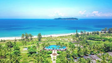 Un resort con piscina, playa y abundante vegetación.