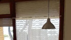 Un comedor con mesa de vidrio, sillas blancas, una lámpara colgante y una planta en maceta.
