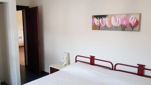 Un dormitorio con una cama, una mesita de noche, un cuadro y una puerta que da a otra habitación.