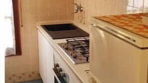 Cocina compacta con armarios blancos, estufa, horno y refrigerador.
