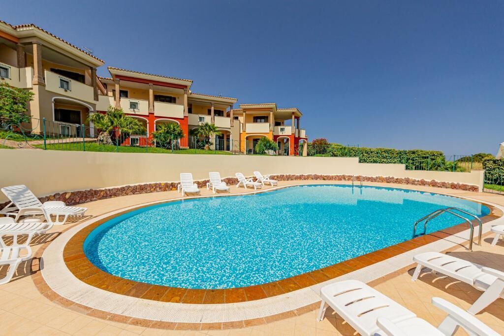 Una piscina con lettini e, sullo sfondo, un edificio con numerosi balconi.
