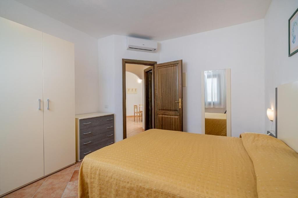 Een slaapkamer met een bed, een kledingkast, een dressoir en een deur naar een andere kamer.