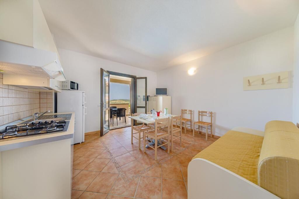A compact kitchen with a gas stove, a microwave, and a refrigerator. There is a dining area with a table and chairs, and a sofa.