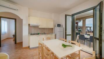 Una cucina compatta con mobili bianchi, un forno a microonde e una zona pranzo con tavolo bianco e sedie in vimini.