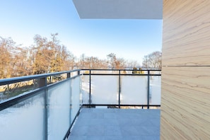 Un balcon doté d’une balustrade en verre, offrant une vue sur les arbres et un ciel dégagé.