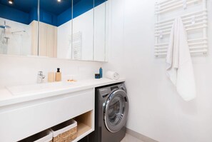 Une salle de bain moderne Ă©quipĂ©e dâun lave-linge intĂ©grĂ©, dâun grand miroir et dâun porte-serviettes.