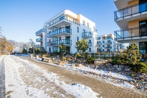 Moderni kerrostalo, jossa on useita parvekkeita, päällystetty kävelyreitti ja lumipeitteinen maa.
