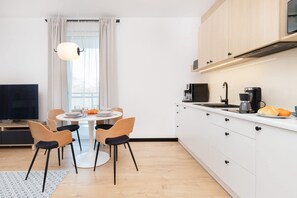 Eine moderne Küche mit weißen Schränken, einem Esstisch mit Stühlen, einem Fernseher und einer Kaffeemaschine.