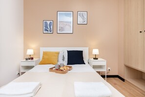 A hotel room with a bed, two bedside tables, a tray with breakfast items, and three framed pictures on the wall.