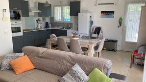 Moderni keittiö, jossa on harmaat kaapit, ruokapöytä tuoleineen sekä sohva, jossa on kuvioituja koristetyynyjä.