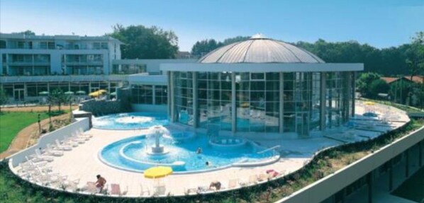 A modern hotel with a swimming pool, a glass-enclosed structure, and a landscaped area with lounge chairs.