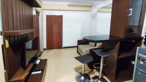 A compact living space with a kitchenette, a small dining area with a bar counter, and a television on a wooden stand. - Lily Room at Apartment Cibubur Village (Depok)