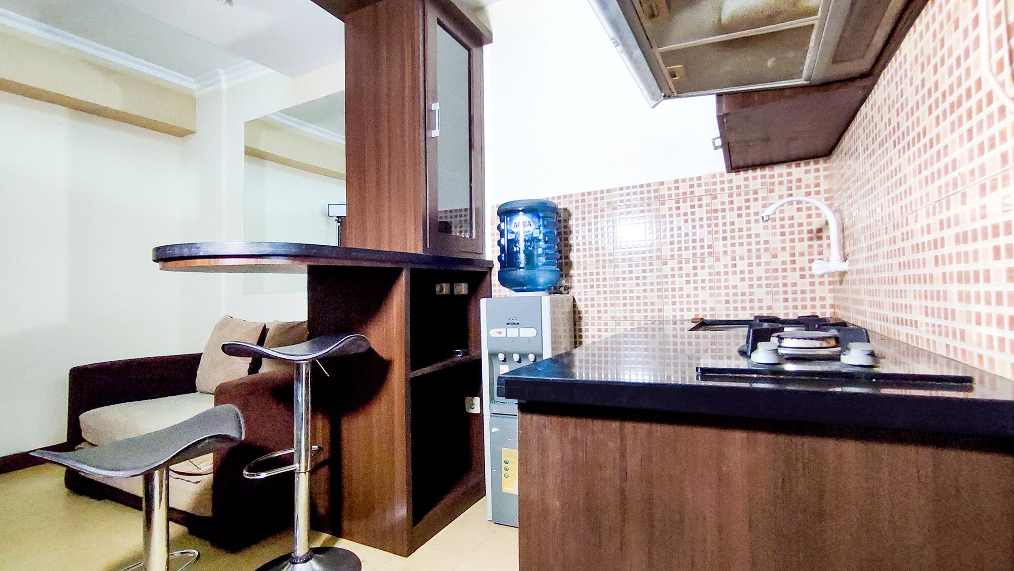 Uma cozinha compacta com um banquinho de bar, um bebedouro e uma geladeira pequena.