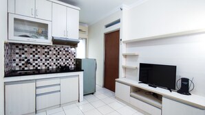 A compact kitchen with white cabinets, a tiled backsplash, a built-in stove, and a refrigerator. - Lily Room at Apartment Cibubur Village (Depok)