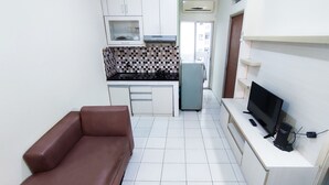 A compact kitchen with white cabinets, a tiled backsplash, a refrigerator, and a television on a stand. - Lily Room at Apartment Cibubur Village (Depok)