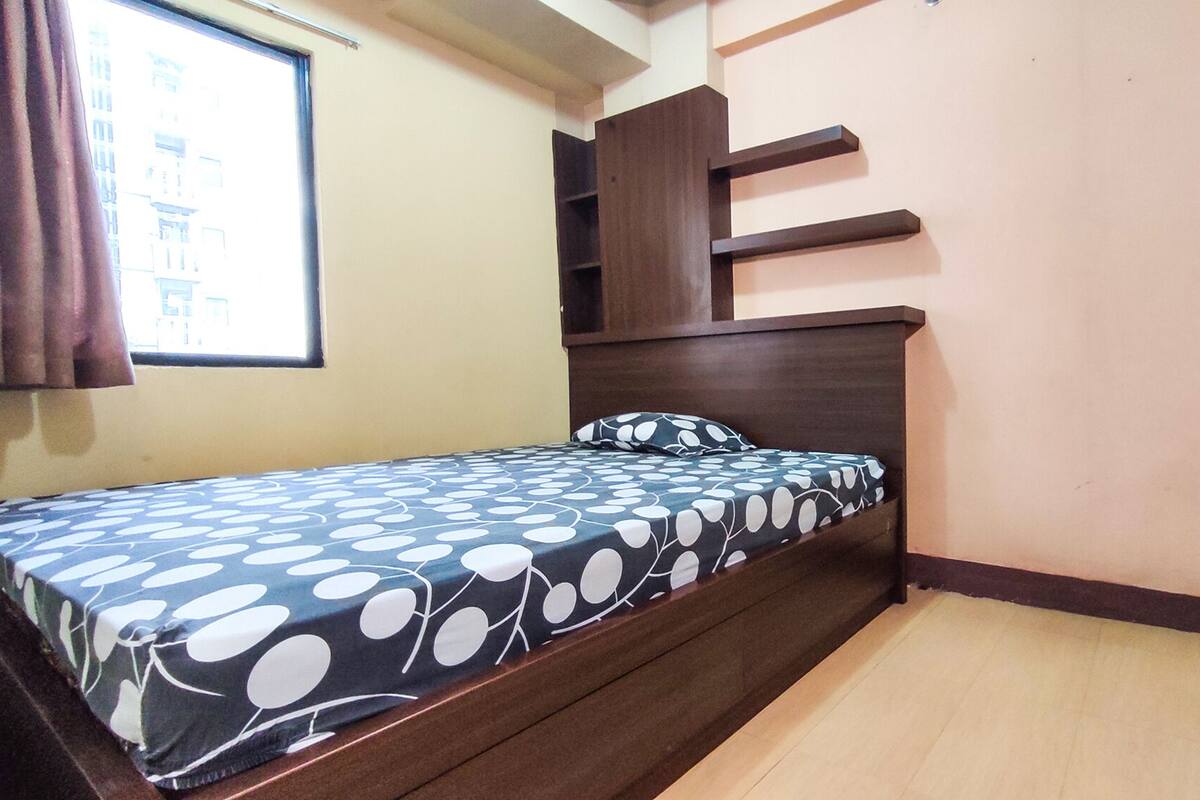 Une chambre à coucher avec un lit, une fenêtre avec des rideaux, une tête de lit en bois et une porte.