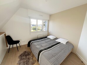A bedroom with two beds, a window, a radiator, a chair, and a fur rug. - DRUIDES 3 - Holiday rentals - Carnac, Morbihan - T5 (Carnac)