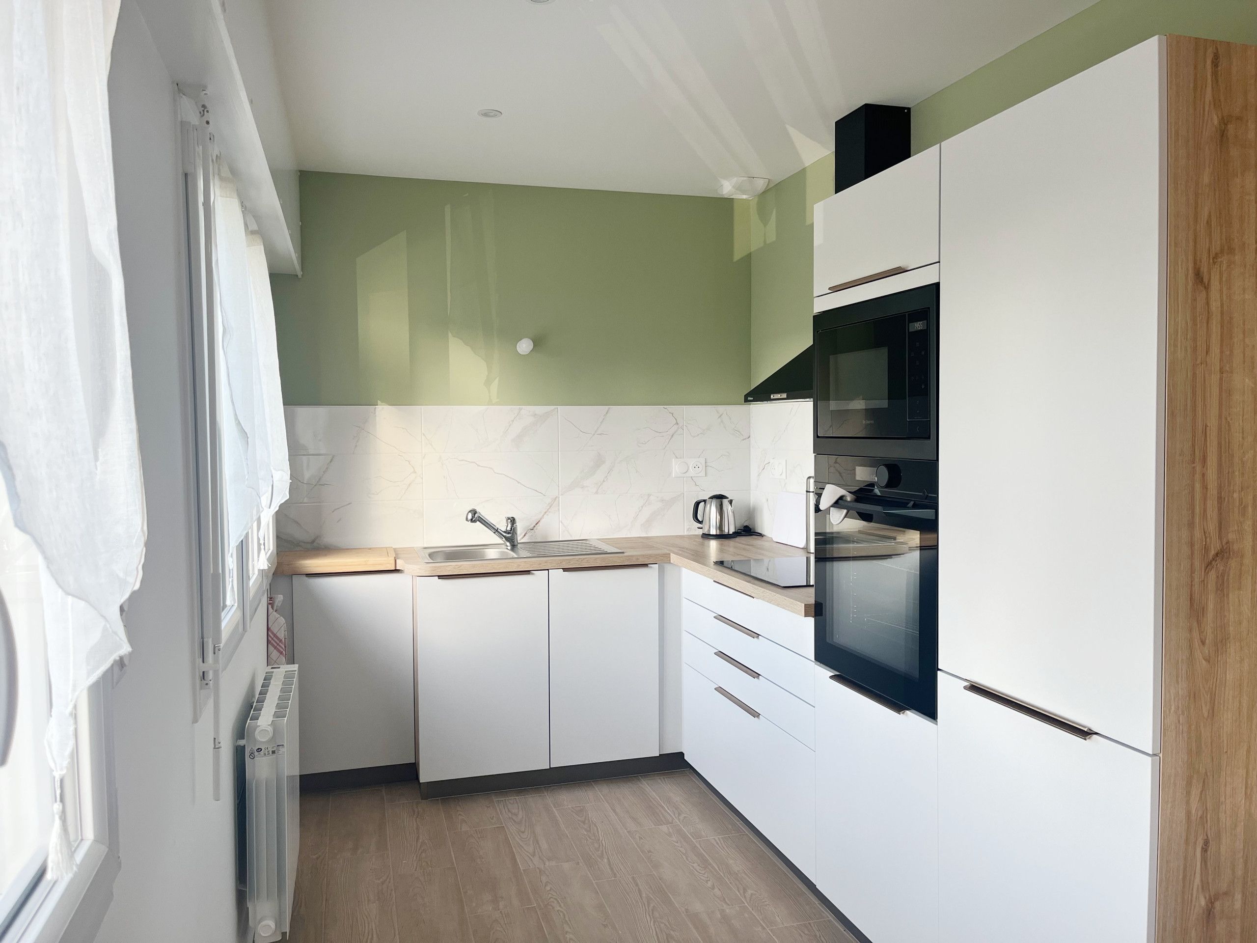 A kitchen with white cabinets, a sink, a kettle, and a microwave.