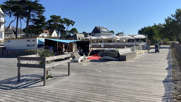 A wooden boardwalk with shops and outdoor seating, a boat, and a signboard. - LES DRUIDES - 2 Chambres, Carnac Plage - T5 (Carnac)